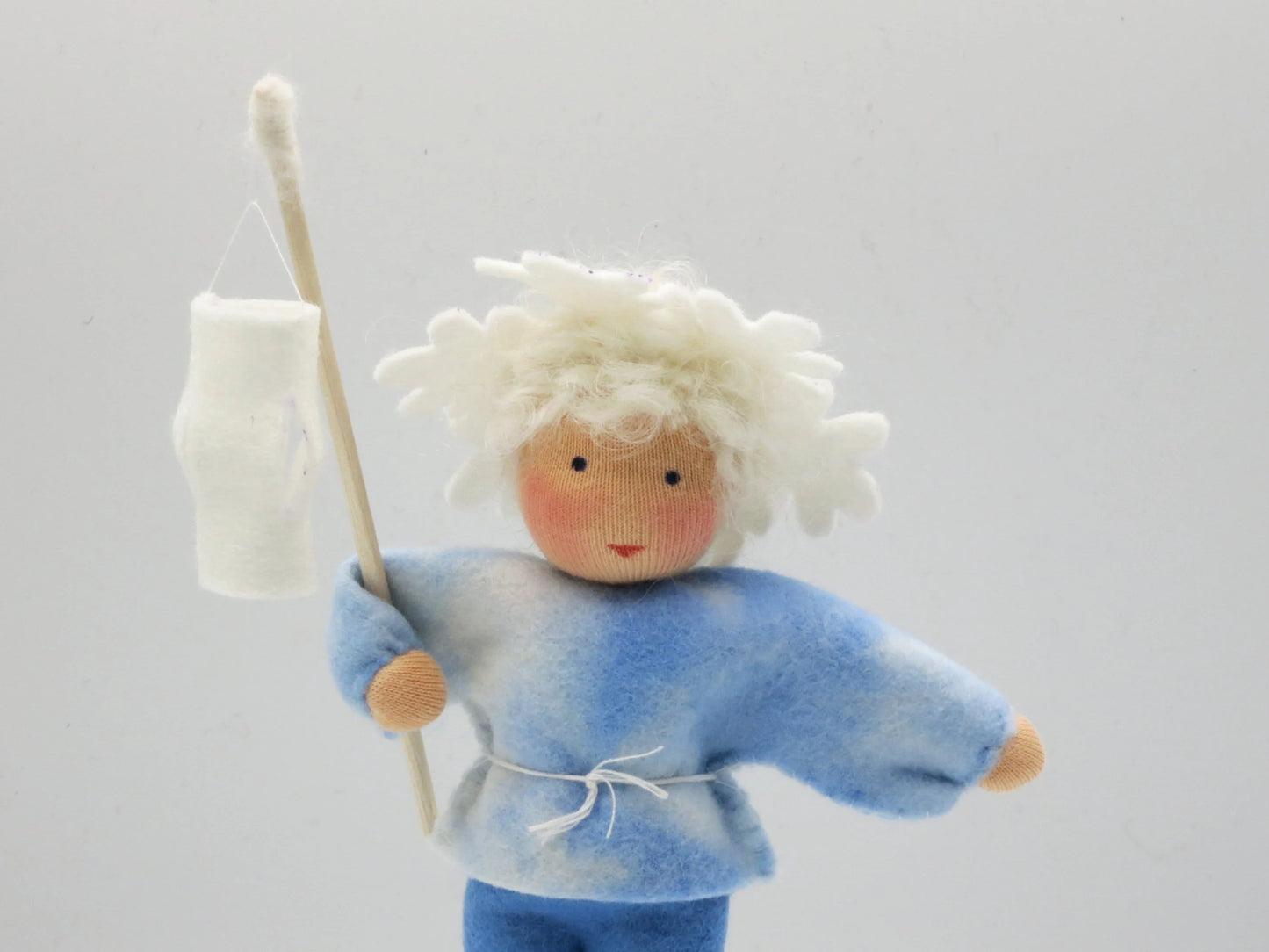 Detailaufnahme des handgefertigten Eiskristall-Blumenkinds mit blauer Filzkleidung und weißer Laterne.