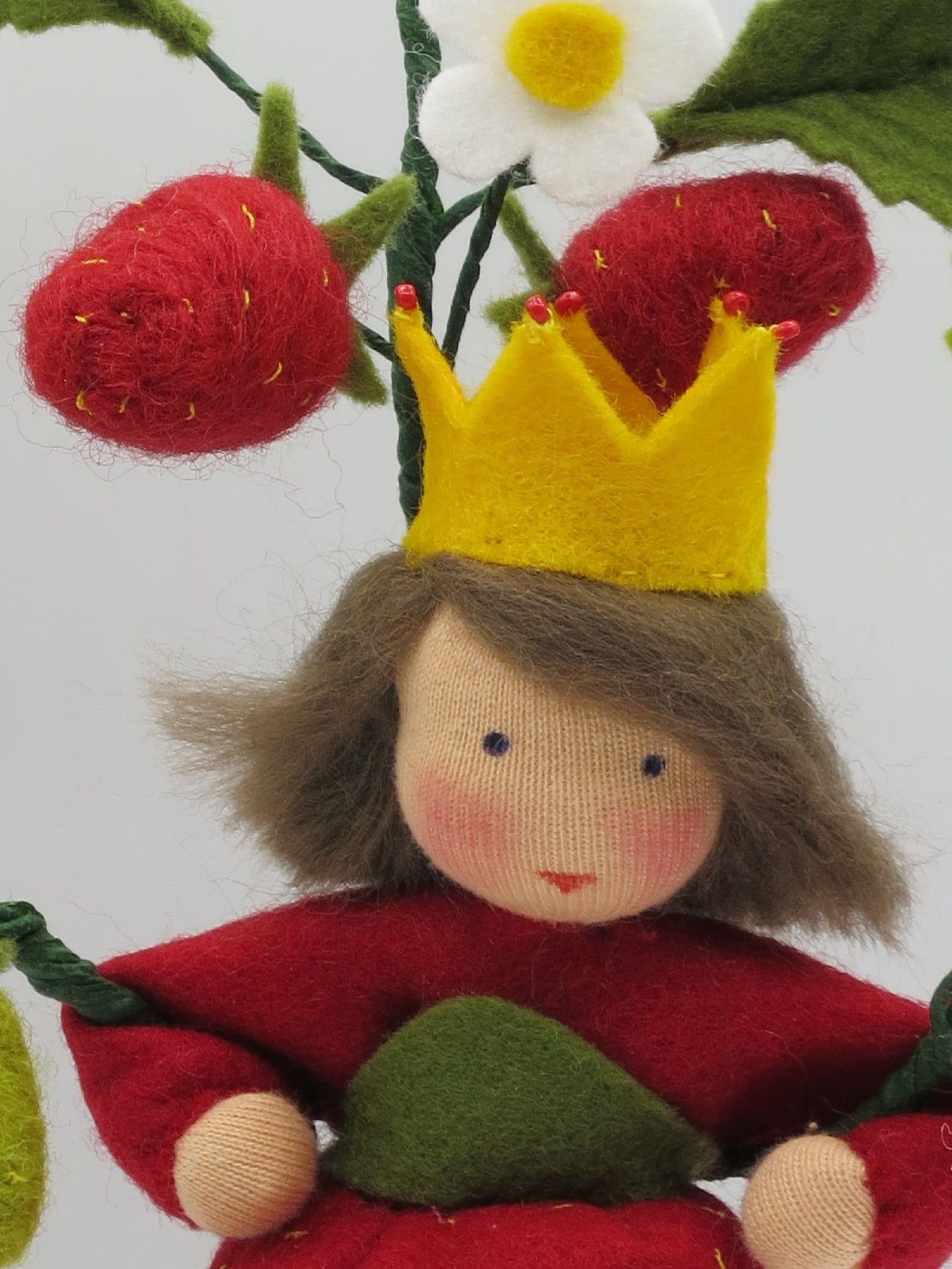 Detailansicht der Erdbeerprinzessin aus Wollfilz mit gelber Krone, weißer Erdbeerblüte und roten Erdbeeren.