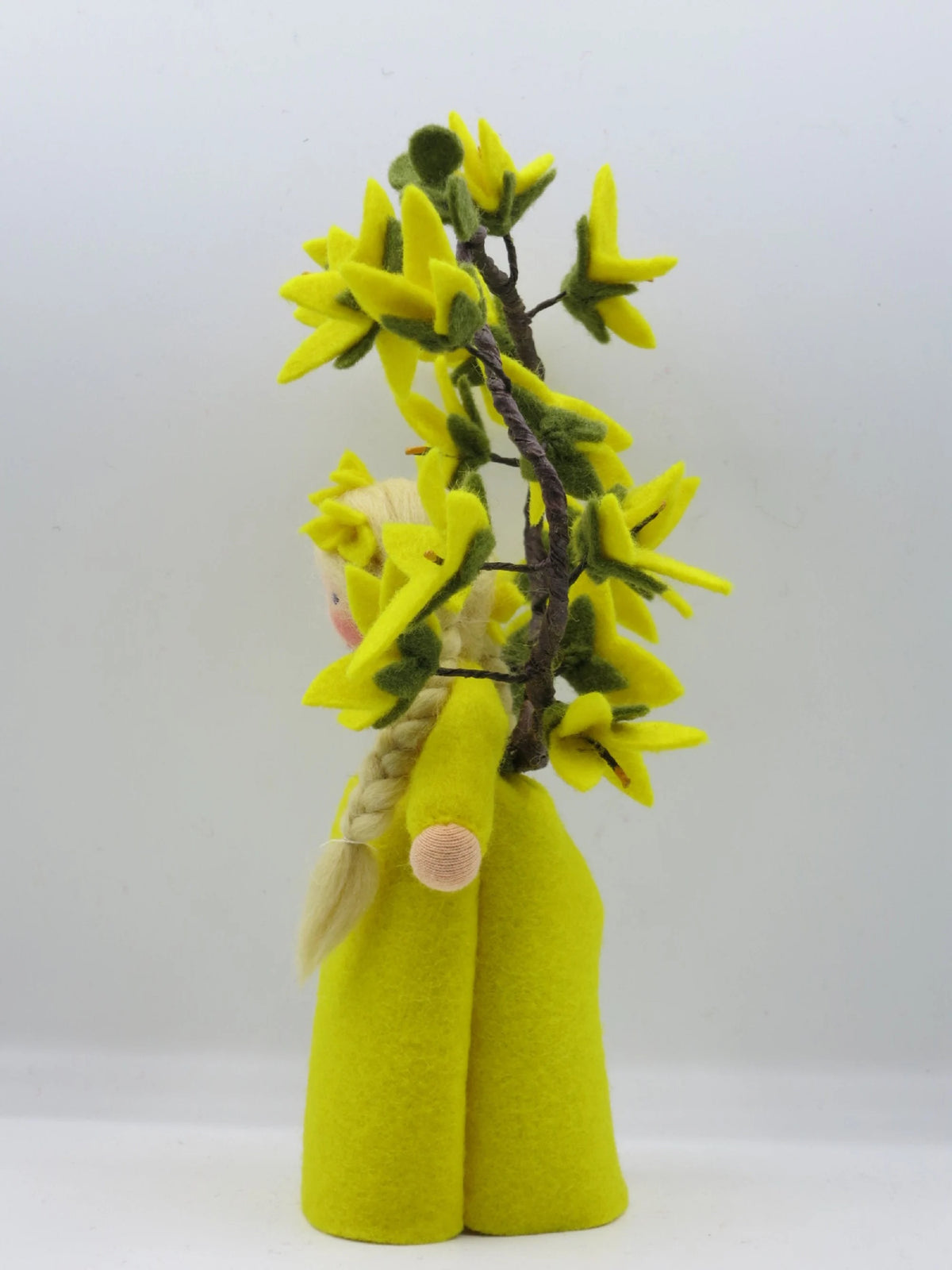 Rückansicht des handgefertigten Forsythien-Blumenkinds aus Wollfilz mit gelbem Kleid, blondem Zopf und Blütenzweig.