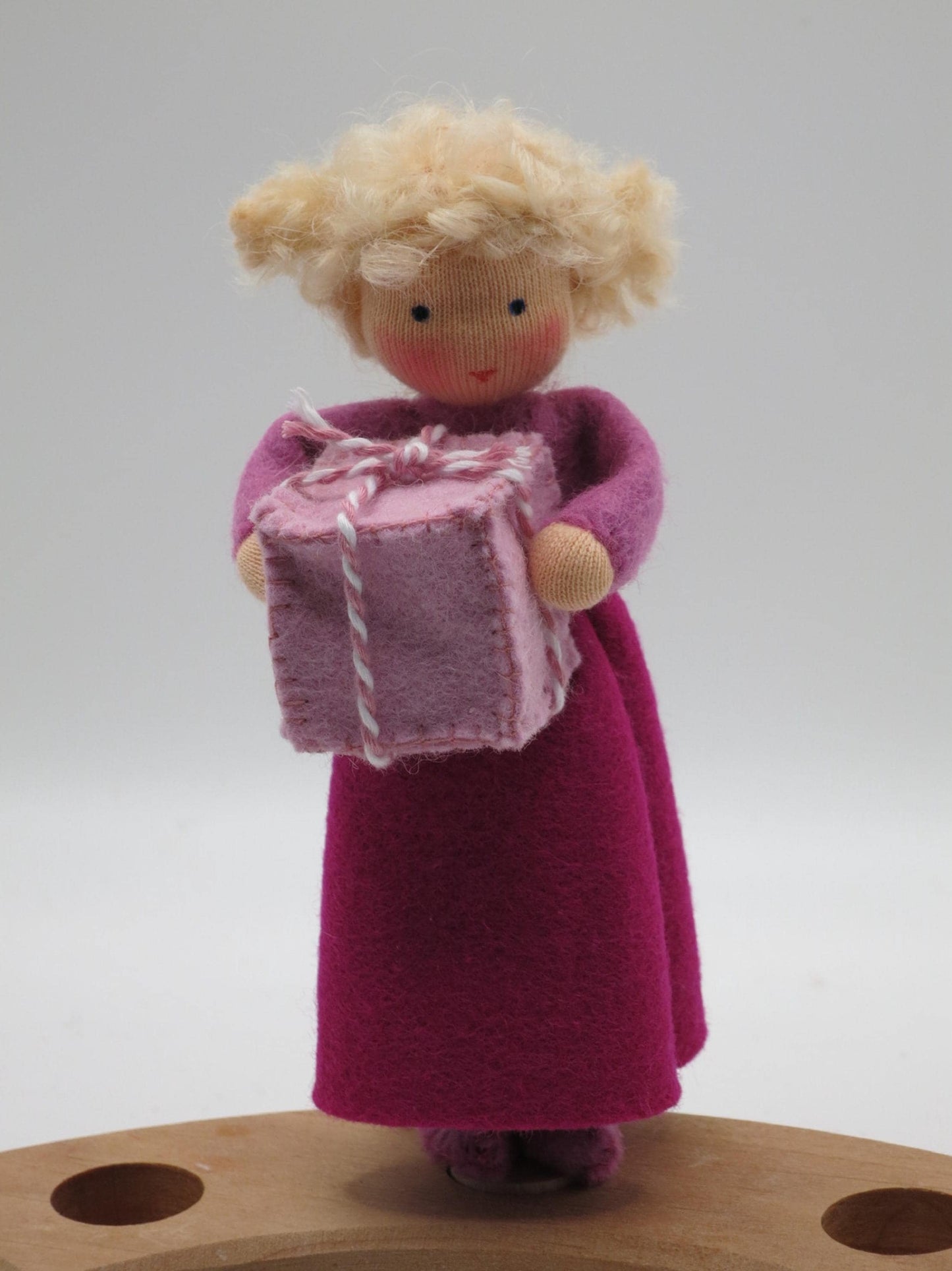 Geburtstagskind aus Wollfilz mit lila Kleid und rosa Geschenk auf einem Holz-Geburtstagsring für den Jahreszeitentisch.