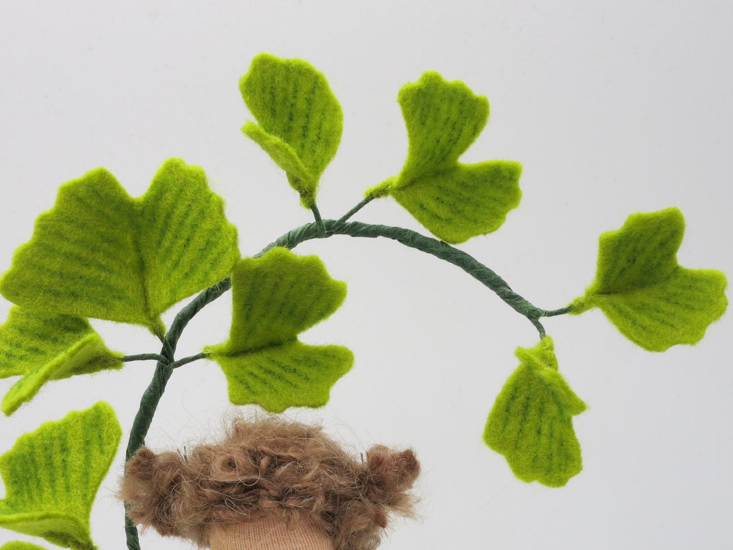 Detailansicht des handgefertigten Ginkgo-Mädchens aus Wollfilz mit Ginkgozweig und fächerförmigen Blättern.