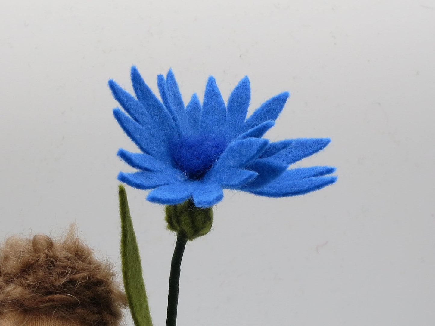Detailansicht der blauen Kornblumen-Blüte aus Wollfilz mit dunkelblauer Mitte und schmalen Strahlenblütenblättern.