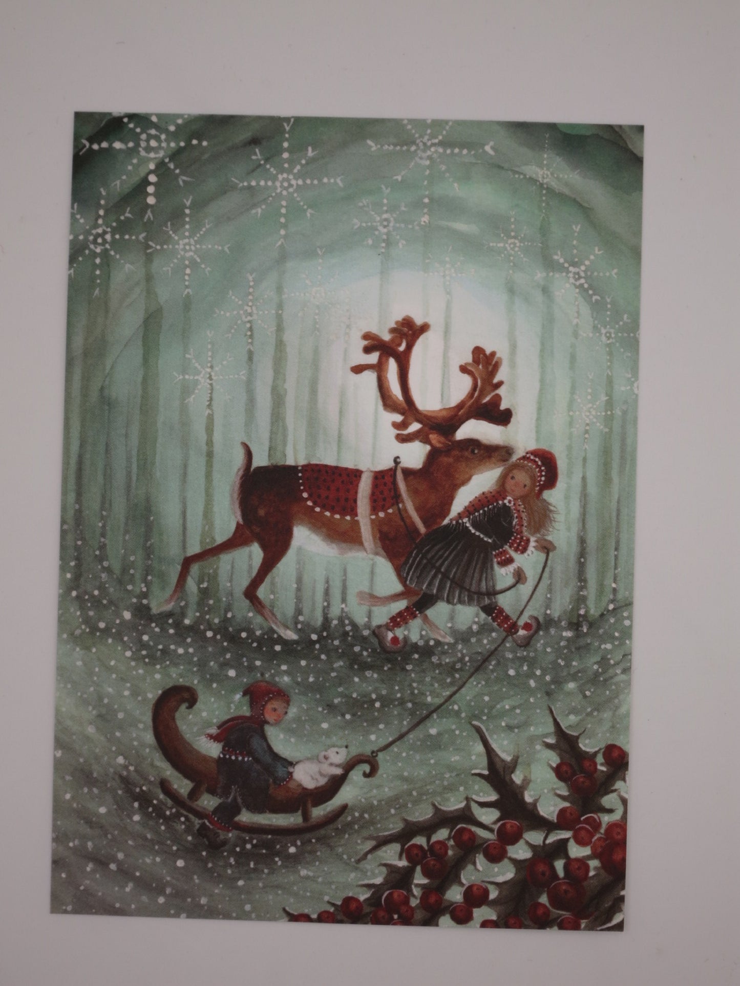 Kunst-Postkarte „Kinder des Nordens“ von Bijdehansje: Mädchen führt Rentier durch Winterwald, Junge zieht Schlitten mit Eisbärenjunges, ideal für den Jahreszeitentisch