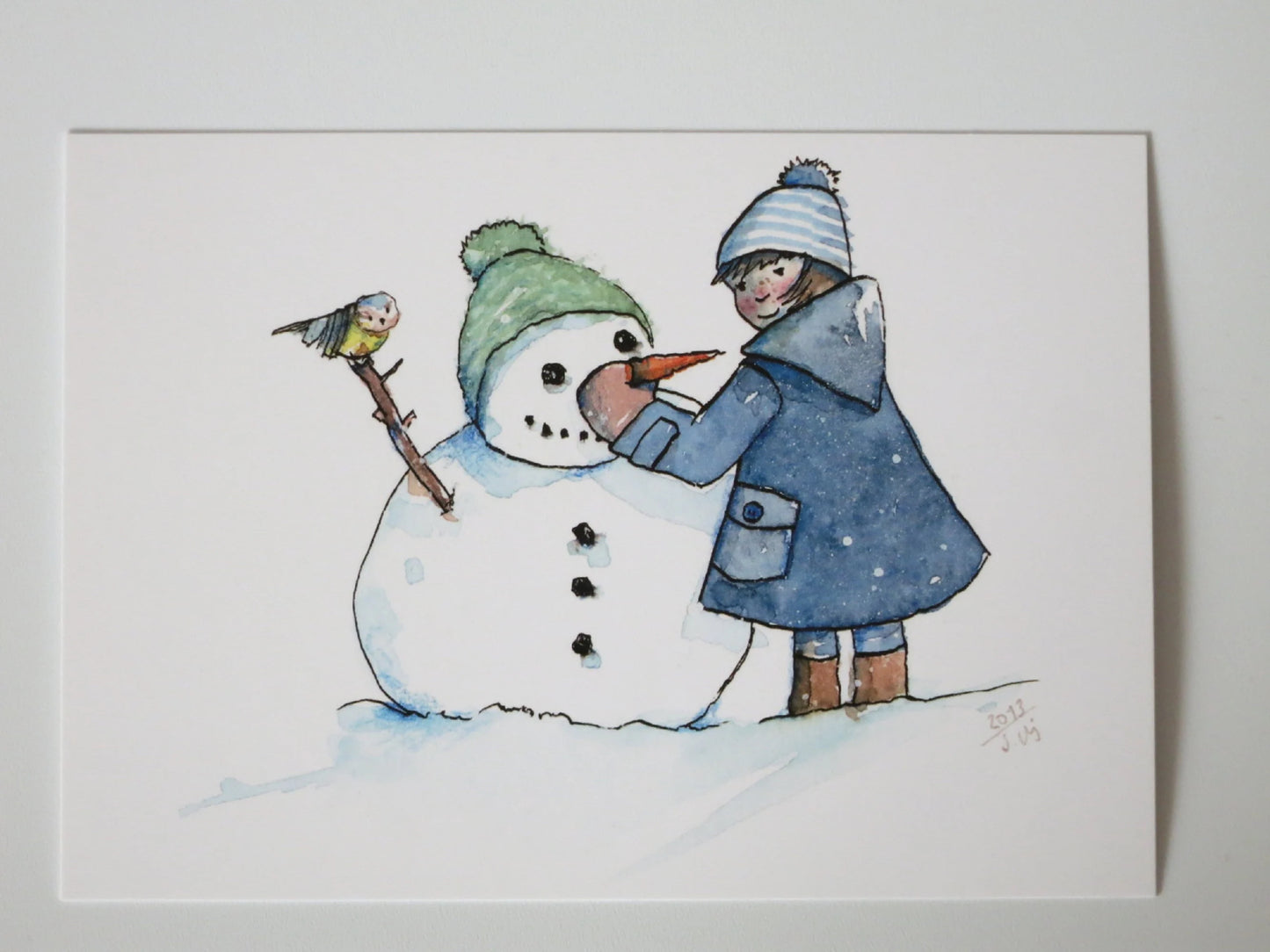 Kunst-Postkarte „Schneemann“ von Stefanie Messing: Kind baut Schneemann mit Karottennase, kleiner Vogel schaut zu, Postkarte für Kinder