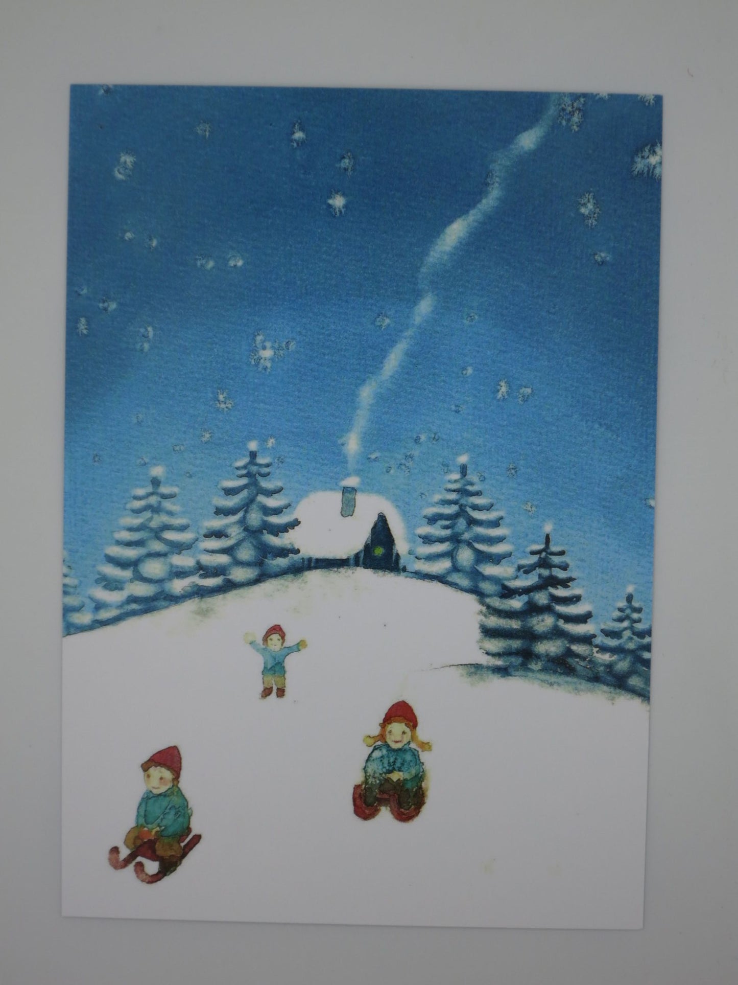 Postkarte Schlittenfahrt von Anna Hunold, Kinder rodeln im Schnee vor Haeuschen mit rauchendem Schornstein