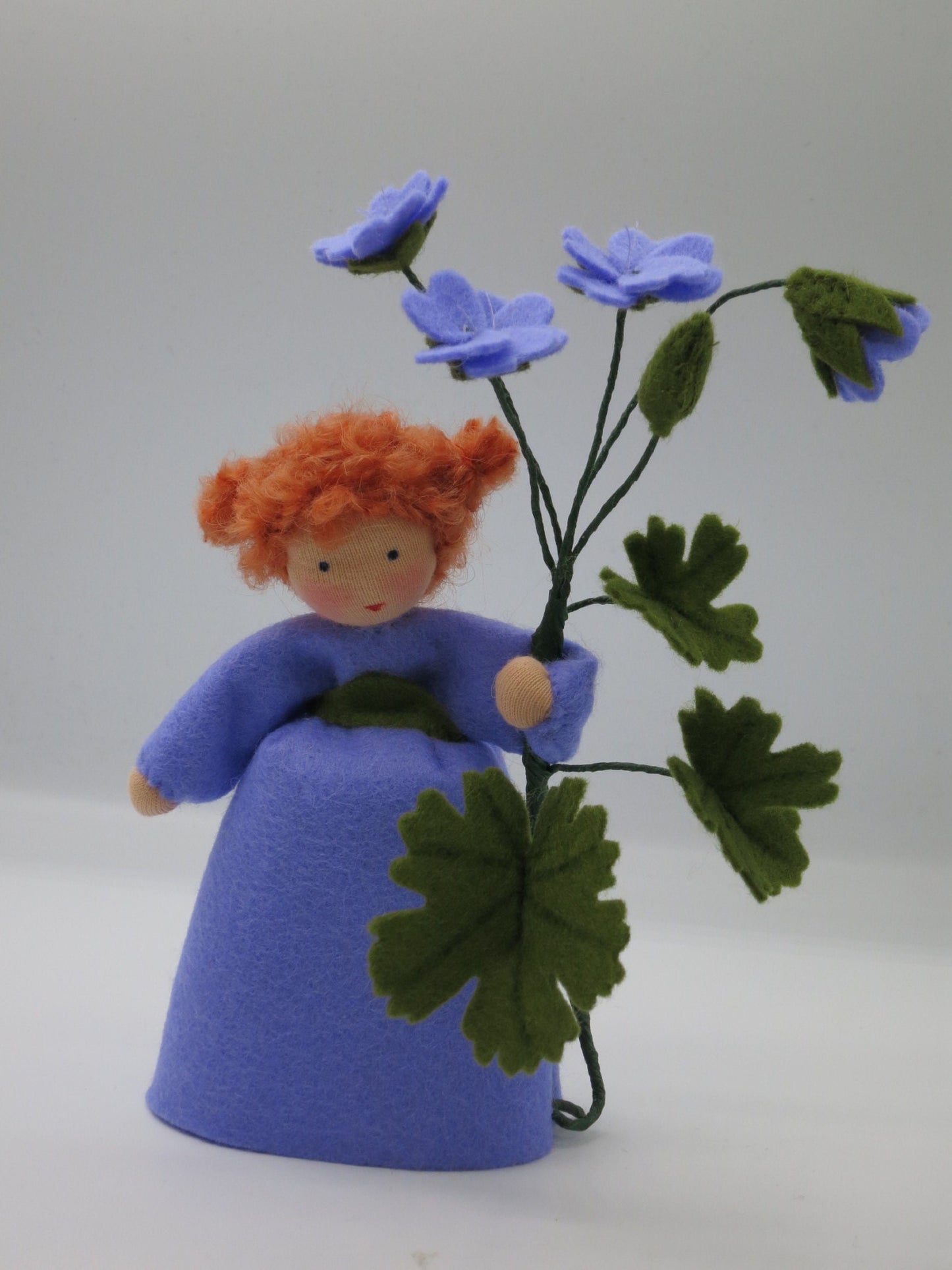 Storchschnabel-Blumenkind aus Wollfilz mit violetten Blüten, Gesamtansicht für den Waldorf Jahreszeitentisch.