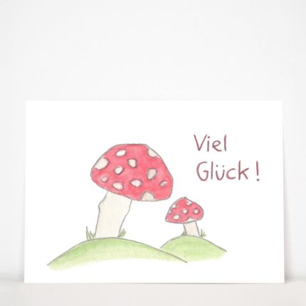 Karte „Viel Glück!“ von Andrea Lienhart: zwei rote Fliegenpilze mit weißen Flecken auf grünen Hügeln, daneben der handgeschriebene Glückwunsch, Postkarte im Querformat