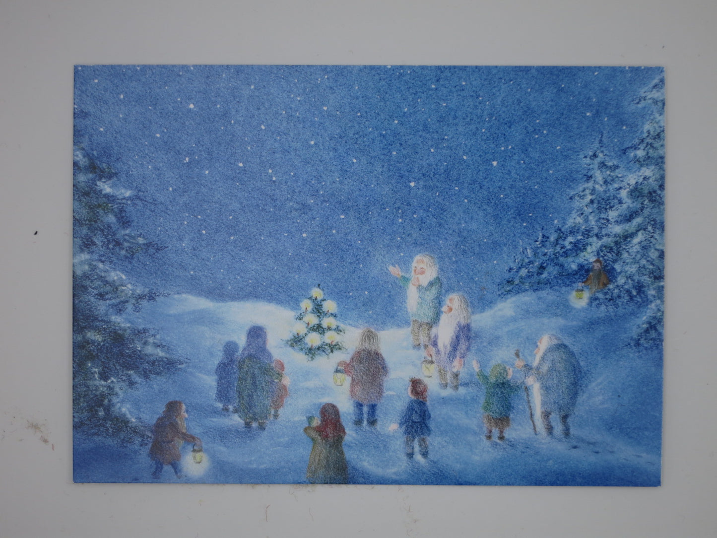 Postkarte Waldweihnacht von Monika Speck, Zwerge mit Laternen versammeln sich um kleines Tannenbaeumchen im Winterwald