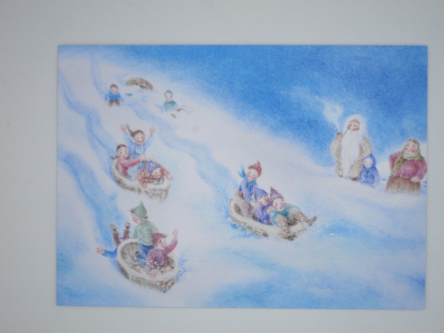 Wichtel-Postkarte „Walnuss-Schalen-Rennen“ von Monika Speck: Wichtelkinder rasen in Walnussschalen den verschneiten Hang hinab, Kunst-Postkarte für Kinder