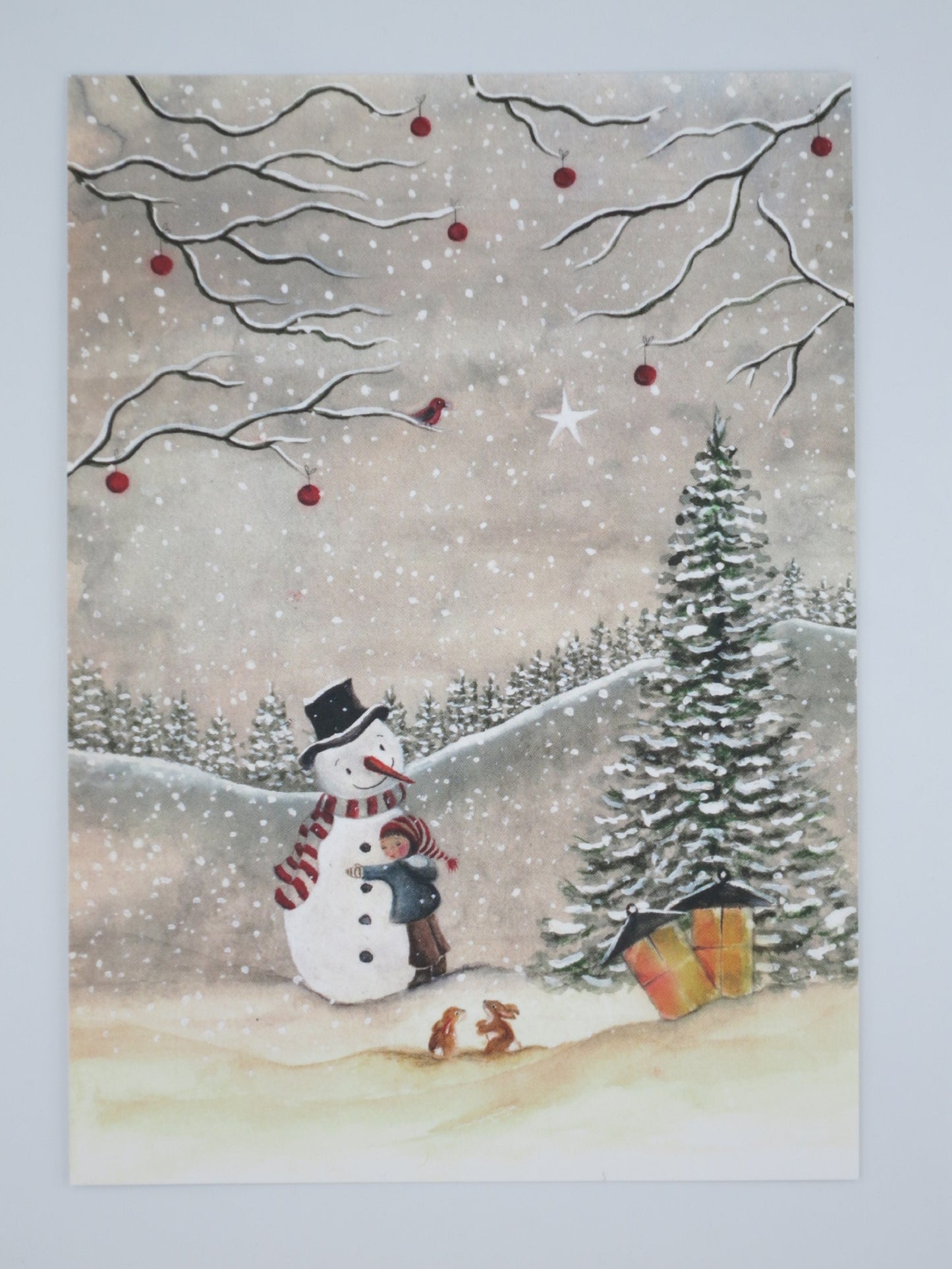 Winterpostkarte für Kinder: Kind umarmt Schneemann neben Tannenbaum mit Geschenken, Rotkehlchen und Hasen, Waldorf Jahreszeitentisch