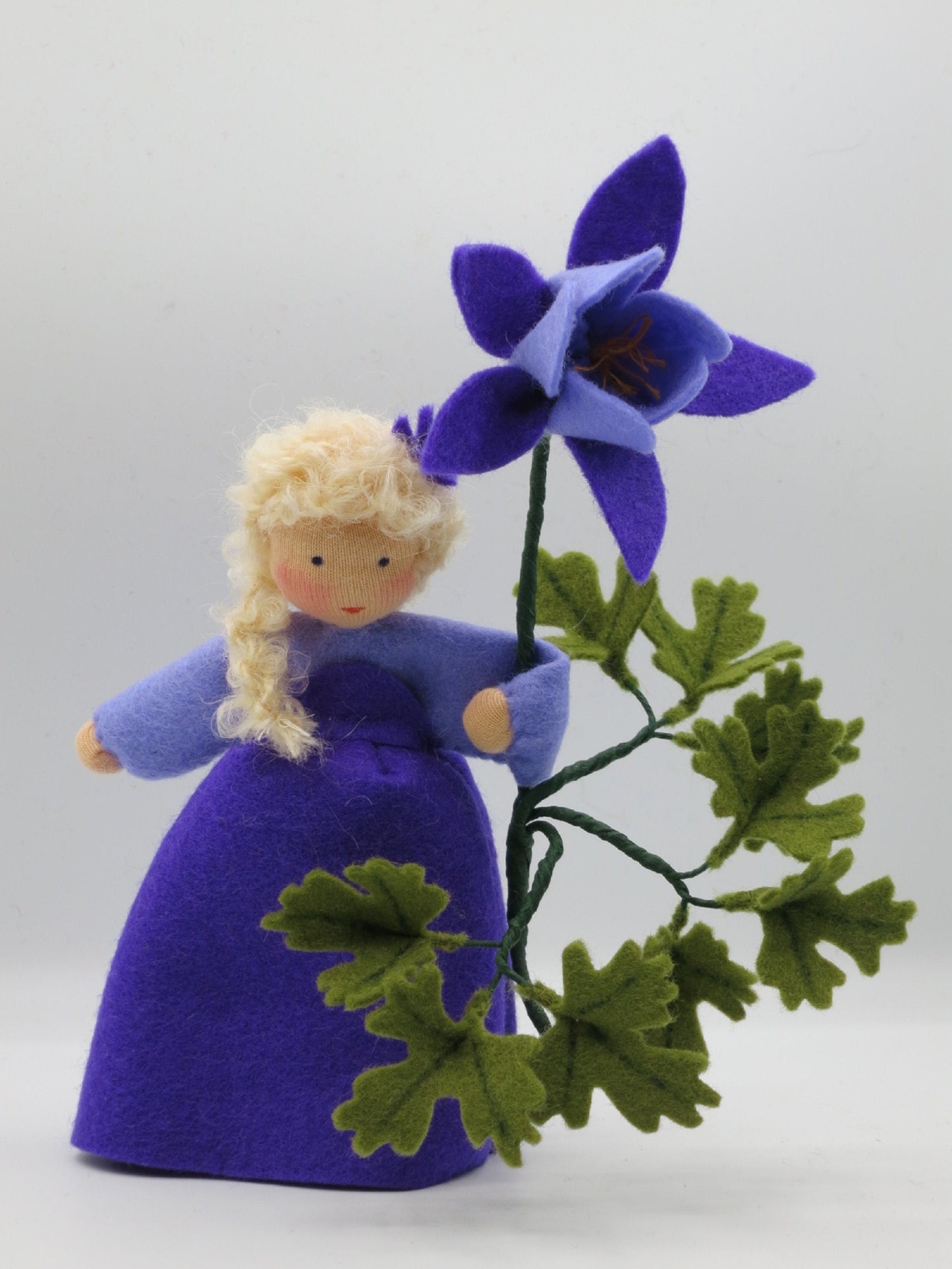 Akelei-Blumenkind mit großer violetter Filzblüte und verzweigtem grünem Blattwerk als Frühlingsdeko.