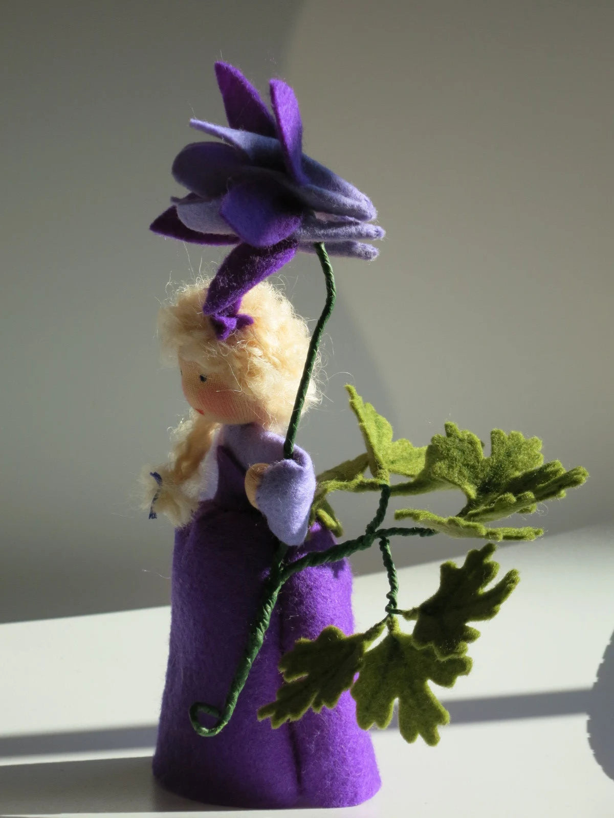 Seitliche Ansicht des violetten Akelei-Blumenkinds mit Filzblüte und Blattzweig im natürlichen Licht.