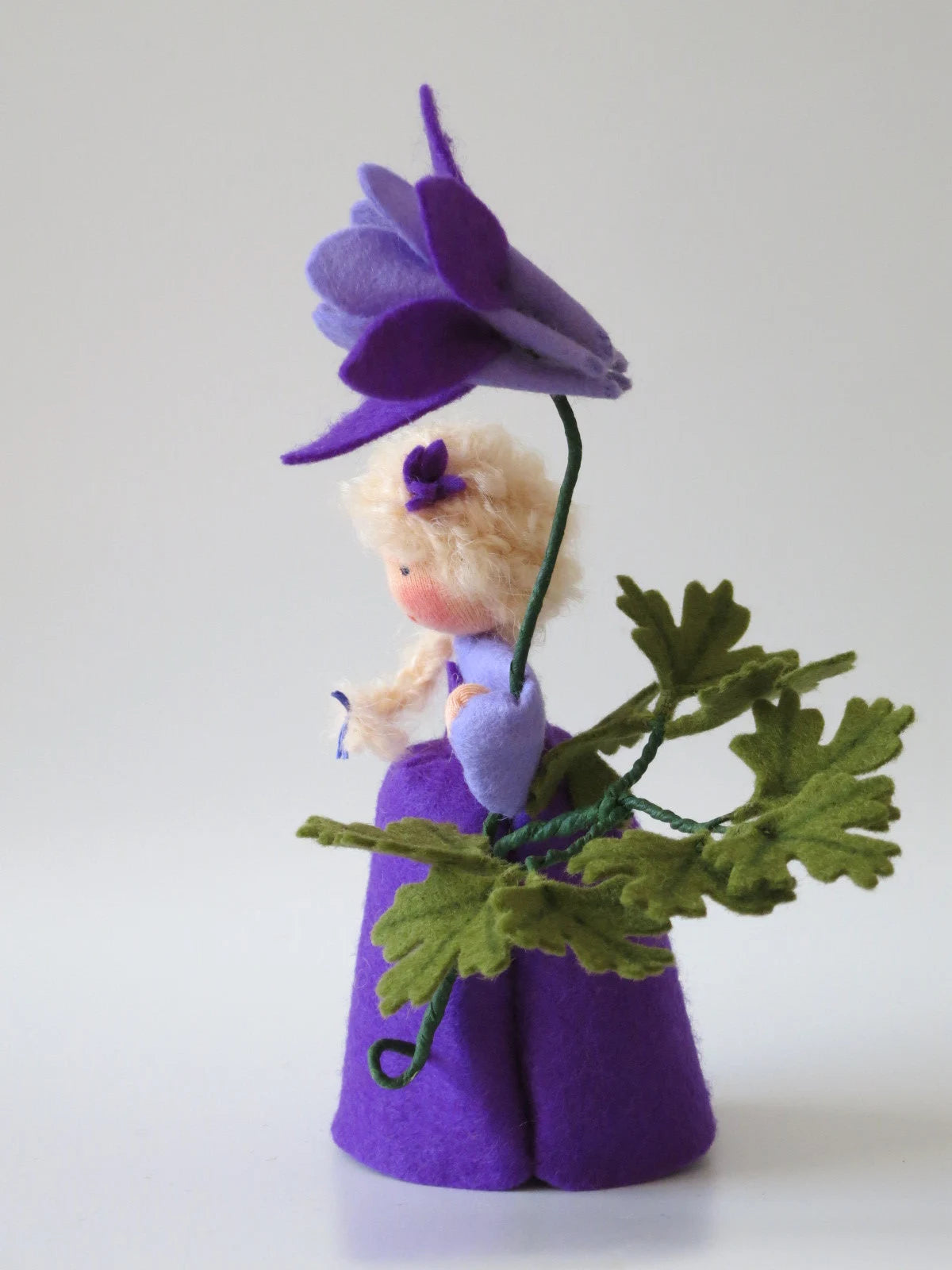 Handgefertigtes Akelei-Blumenkind in Violett mit Blüte und grünen Filzblättern für den Frühlings-Jahreszeitentisch.