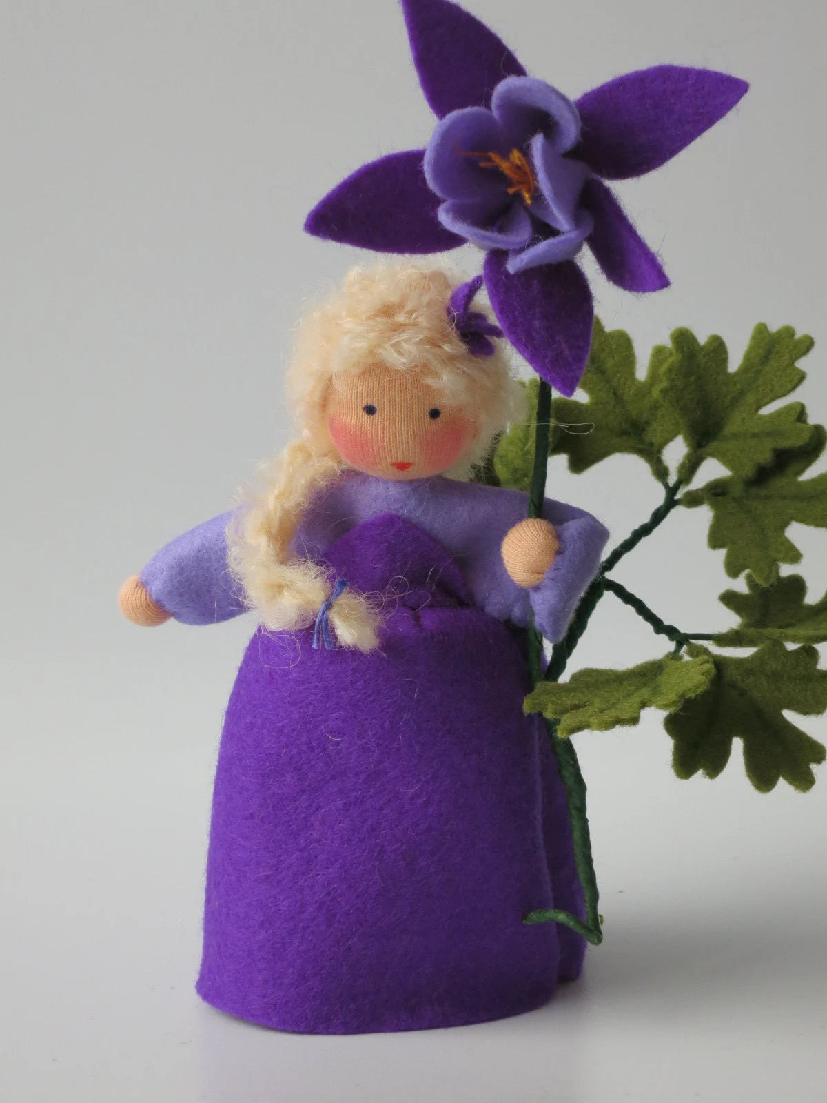 Akelei-Blumenkind im violetten Filzkleid mit großer Blüte und grünen Blättern für den Waldorf Jahreszeitentisch.