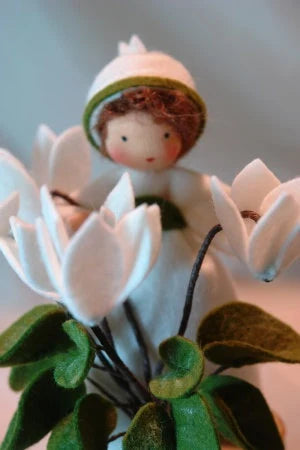 Porträt des handgefertigten Alpenveilchen-Blumenkinds zwischen weißen Filzblüten für den Frühlings-Jahreszeitentisch.