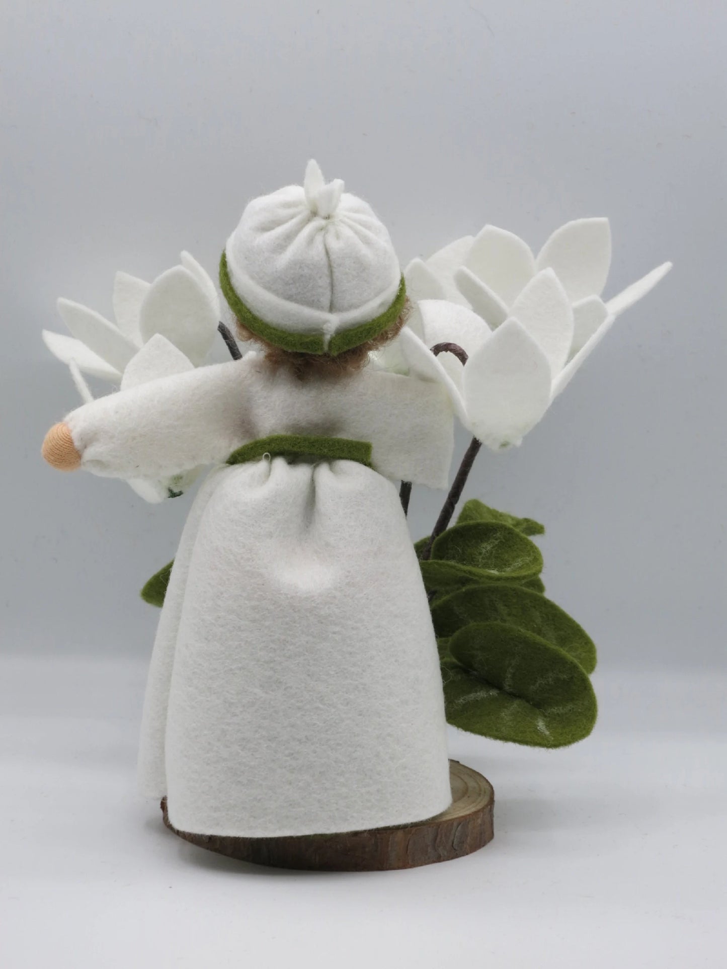 Rückansicht des weißen Alpenveilchen-Blumenkinds mit grünem Filzband, Blüten und Blättern auf Holzsockel.