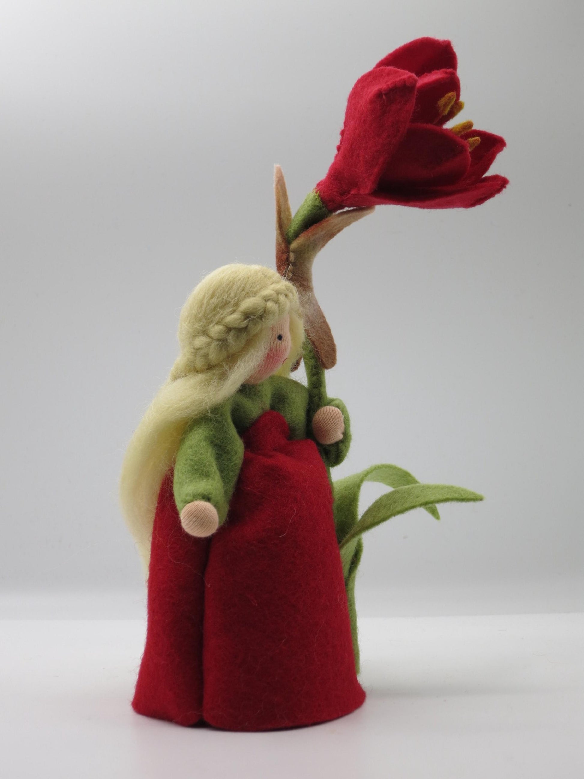 Seitliche Ganzfigur des Amaryllis-Blumenkinds im roten Filzkleid mit grünen Ärmeln und hoher Blüte.