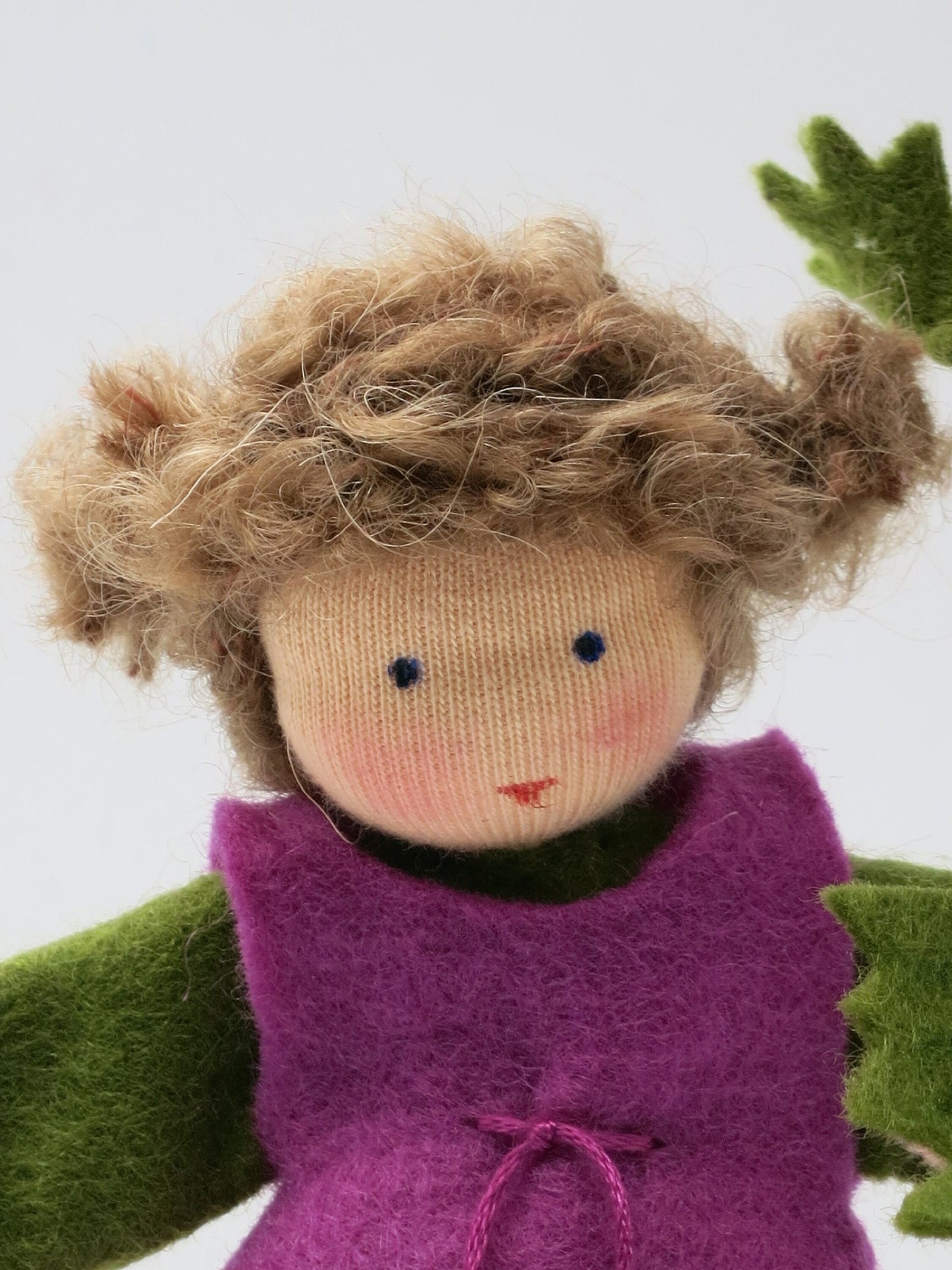 Porträt des handgefertigten Anemone-Blumenkinds als Mädchen mit braunem Wollhaar und violett-grüner Filzkleidung.