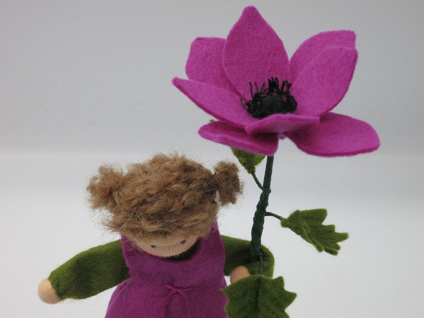 Detailansicht des Anemone-Blumenkinds als Mädchen mit violetter Filzblüte und dunkler Blütenmitte.