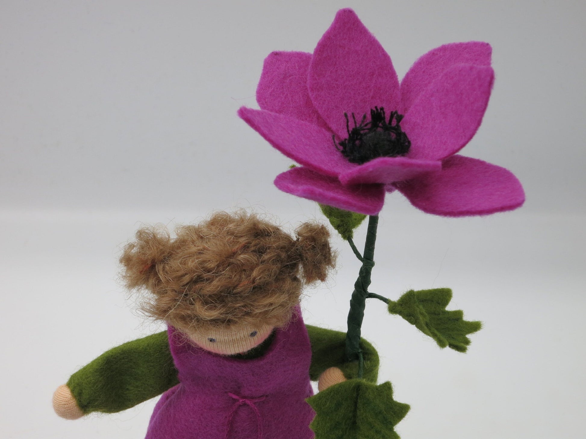 Detailansicht des Anemone-Blumenkinds als Mädchen mit violetter Filzblüte und dunkler Blütenmitte.