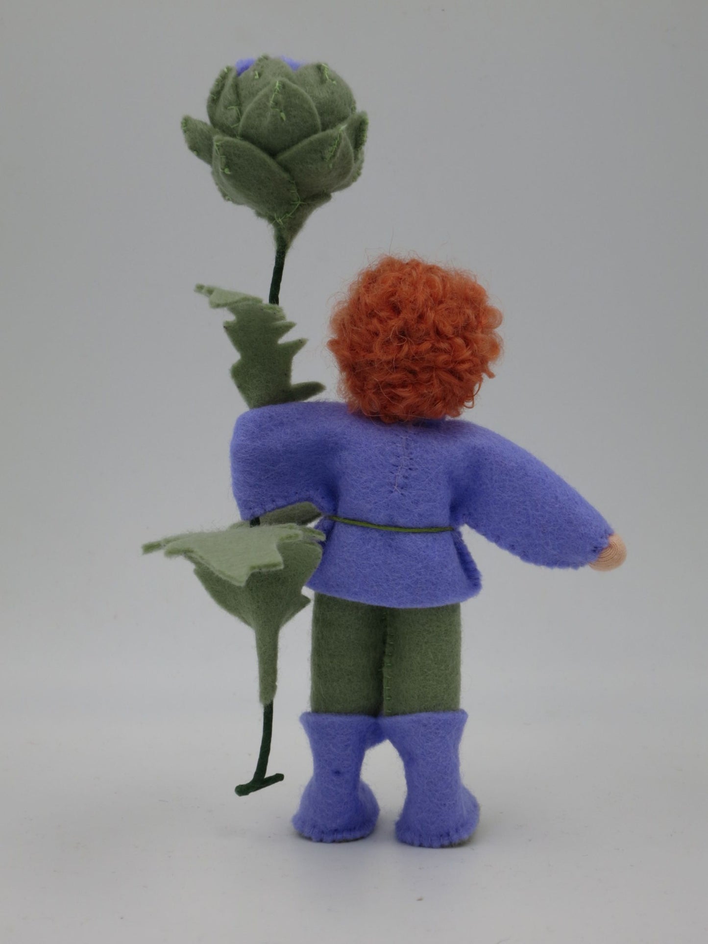 Rückansicht des Artischocken-Blumenkinds Art. SO152 mit lockigem rotem Wollhaar, violetter Jacke und grüner Artischocke.