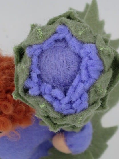 Draufsicht auf die handgearbeitete violette Filzblüte mit grünen Artischockenblättern am Blumenkind Art. SO152.