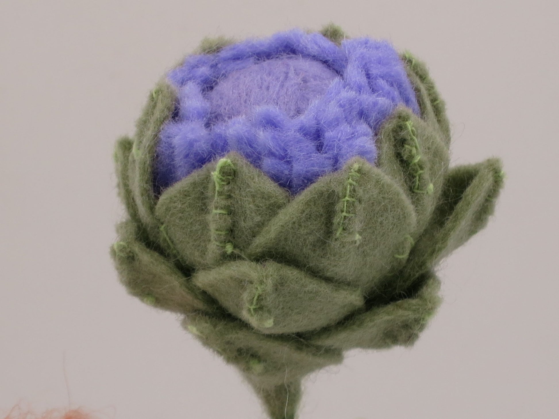 Nahaufnahme der violett-grünen Artischockenblüte aus Wollfilz am handgefertigten Sommer-Blumenkind Art. SO152.