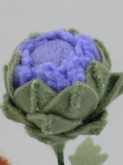 Detailaufnahme der violetten Artischockenblüte aus Filz mit grünen Hüllblättern am Blumenkind Art. SO152.