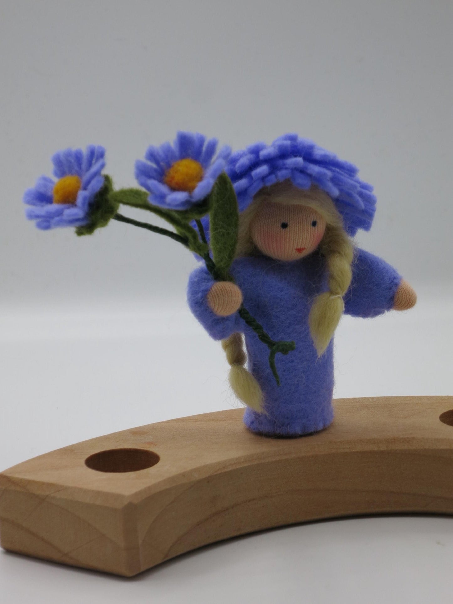 Handgefertigtes Aster-Blumenkind Art. HE54 mit blondem Zopf und violettem Asternzweig auf dem Holz-Geburtstagsring.