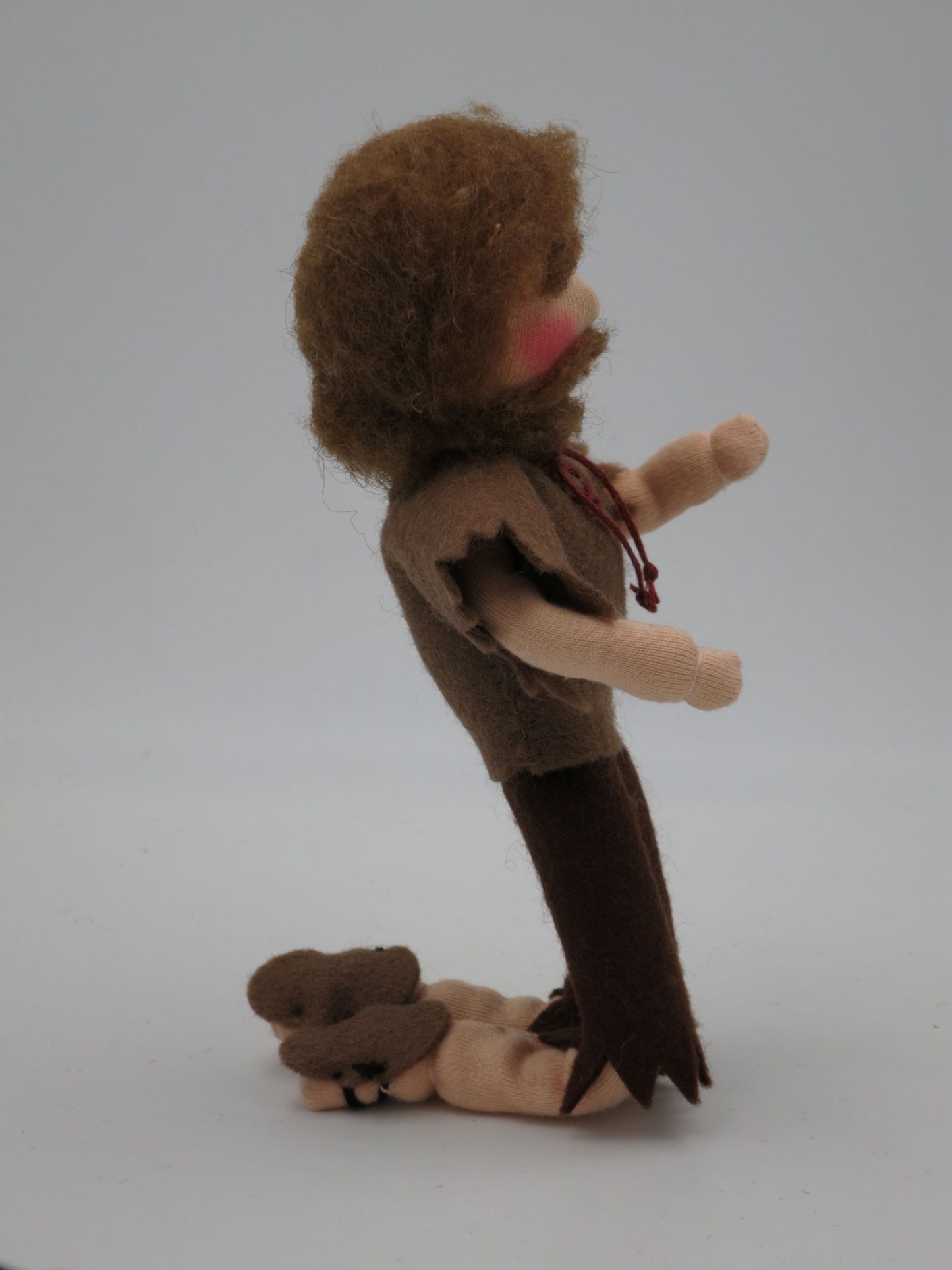 Kniender Bettler Art. HE68 in brauner Filzkleidung von der Seite, mit ausgestreckten Armen und kleinem Stoffbündel.