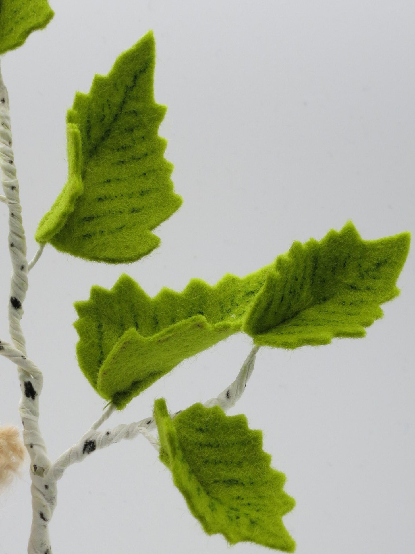 Detailaufnahme grüner Birkenblätter aus Filz an einem weiß-schwarz gestalteten Birkenzweig des Baumkinds Art. FR22.