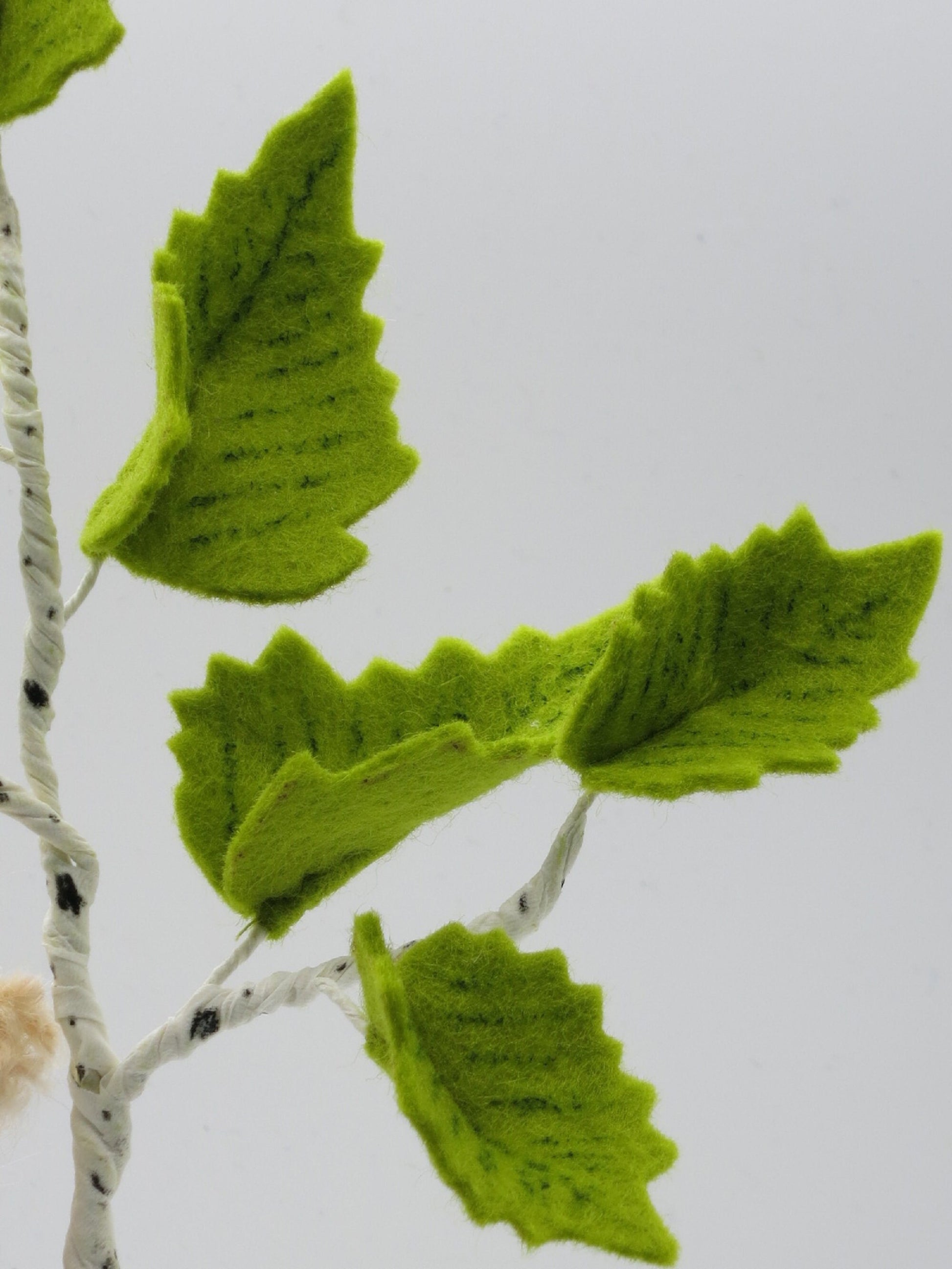 Detailaufnahme grüner Birkenblätter aus Filz an einem weiß-schwarz gestalteten Birkenzweig des Baumkinds Art. FR22.