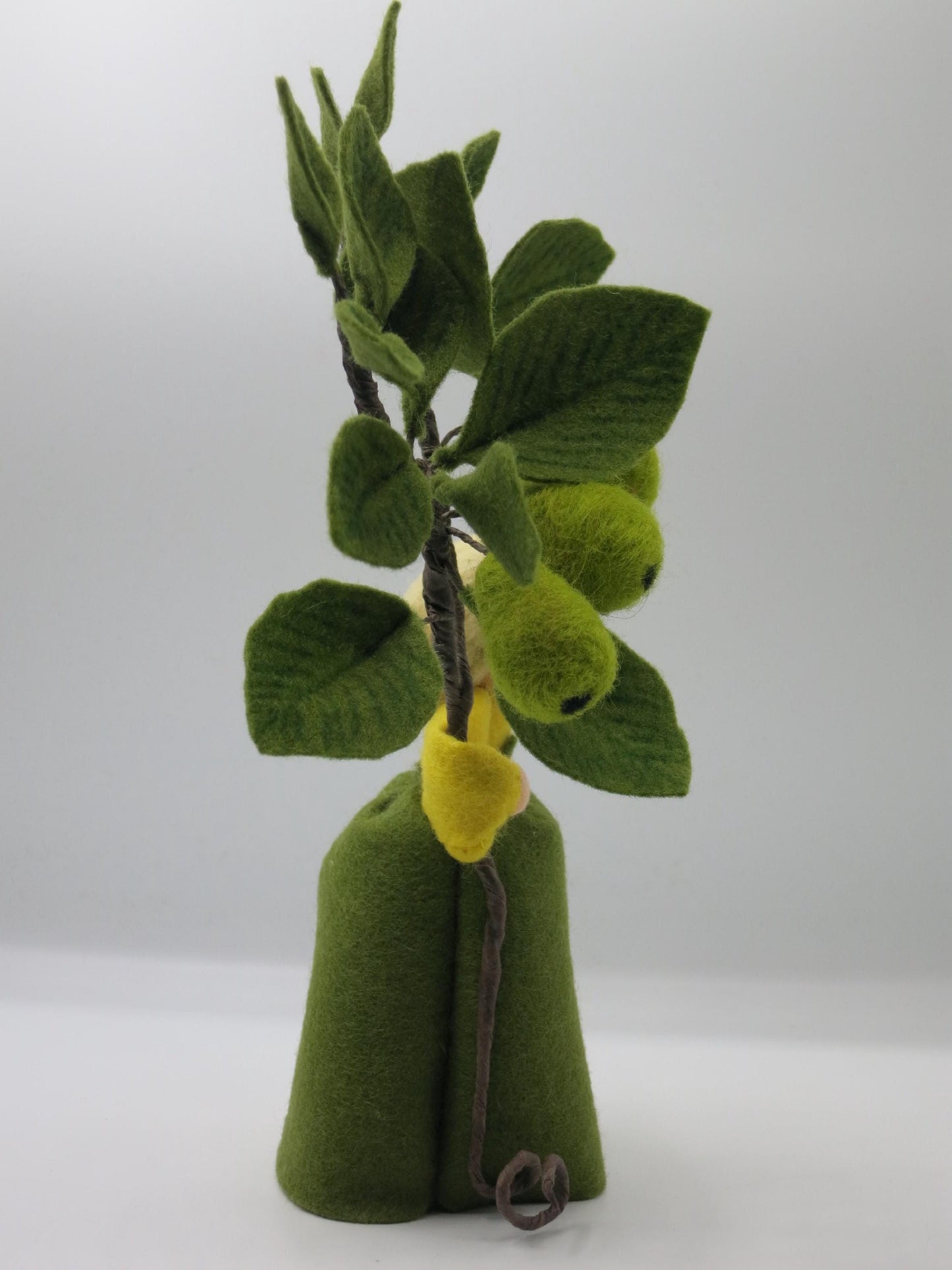 Rückseite des Birnen-Blumenkinds mit grünem Filzkleid und dichtem Zweig aus Birnen und Blättern aus Wollfilz.