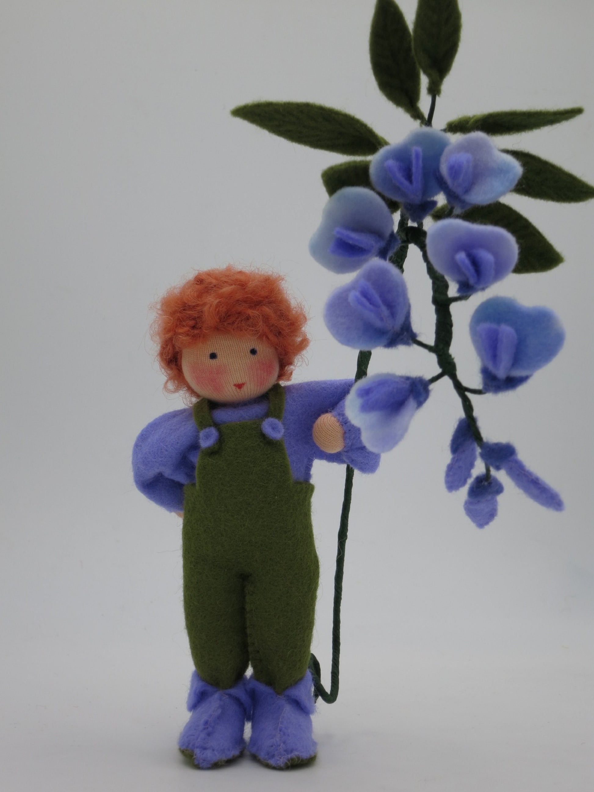 Handgefertigtes Blauregen-Blumenkind mit rotem Wollhaar, grün-violetter Filzkleidung und großem Blütenzweig für den Frühlings-Jahreszeitentisch.