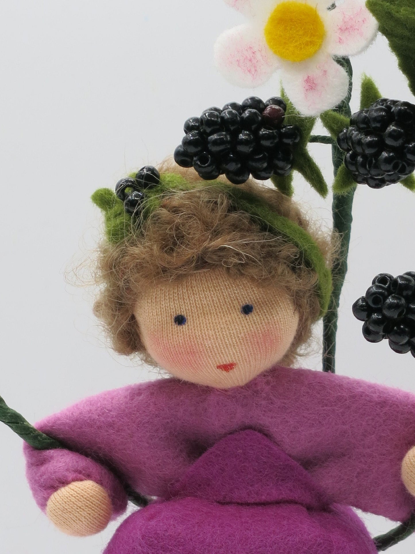 Porträt des Brombeer-Blumenkinds mit braunem Wollhaar, weißen Filzblüten und glänzenden schwarzen Beeren.