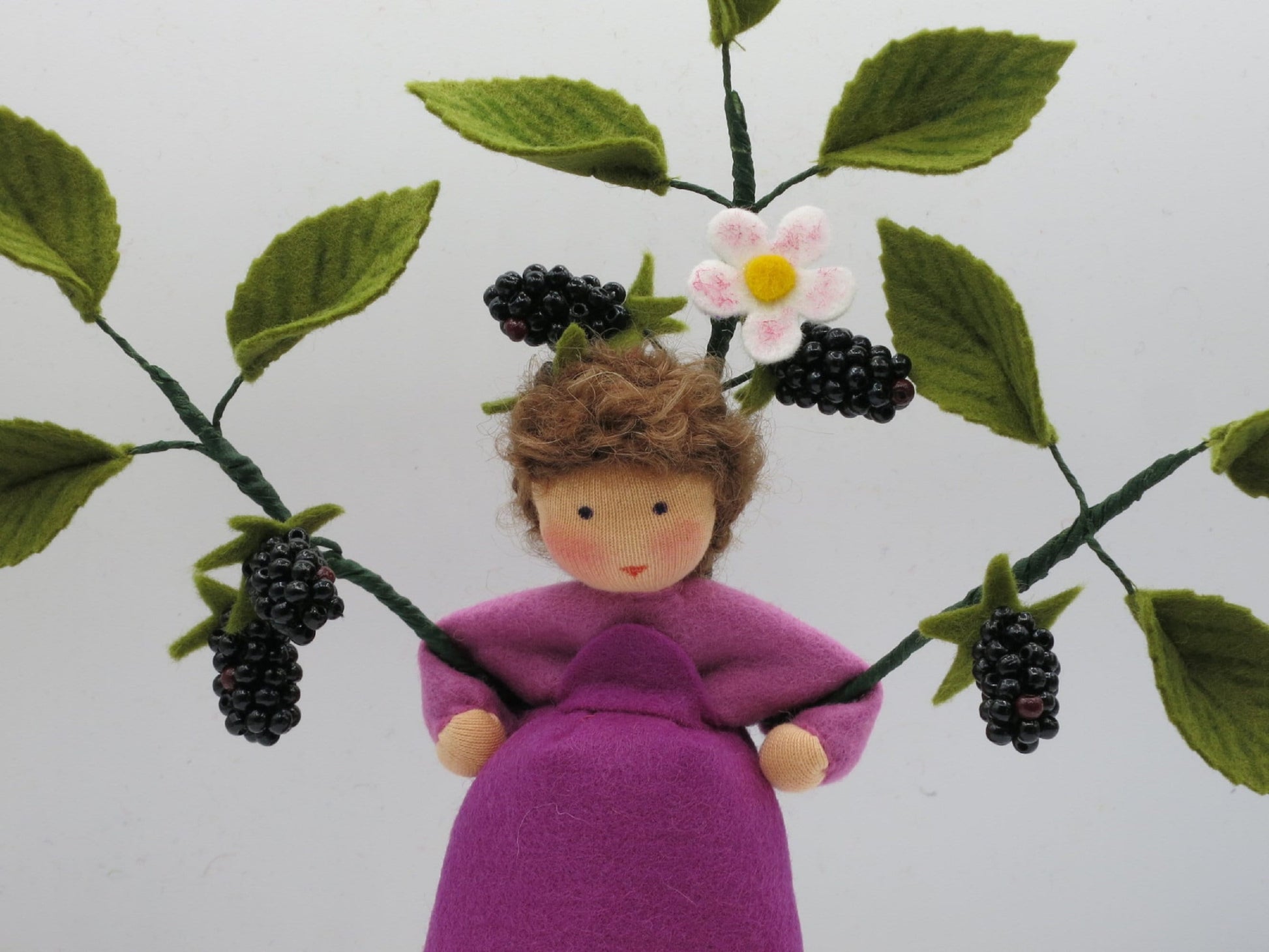 Halbporträt des Brombeer-Blumenkinds zwischen grünen Filzzweigen mit weißen Blüten und schwarzen Beeren.