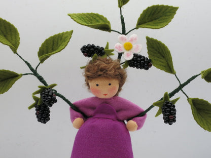 Halbporträt des Brombeer-Blumenkinds zwischen grünen Filzzweigen mit weißen Blüten und schwarzen Beeren.
