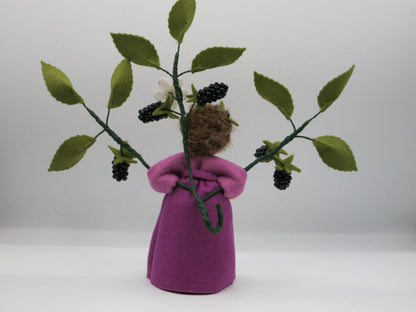 Rückansicht des Brombeer-Blumenkinds mit braunem Wollhaar und ausgebreiteten Brombeerzweigen mit grünen Blättern.