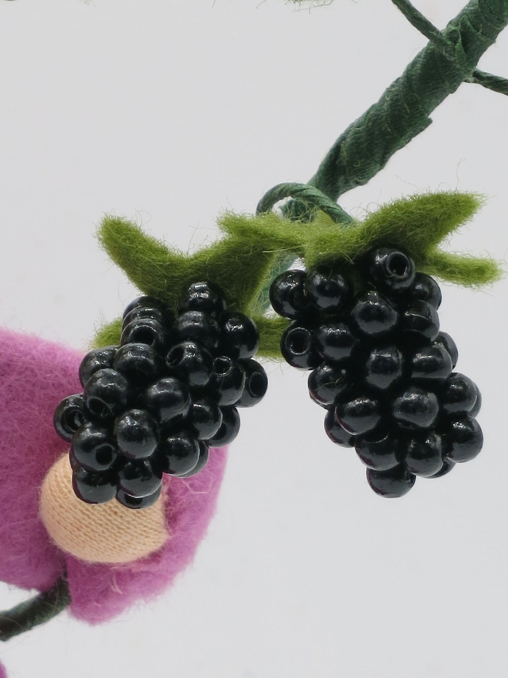 Nahaufnahme zweier schwarzer Brombeerfrüchte am handgefertigten Filzzweig des Brombeer-Blumenkinds.