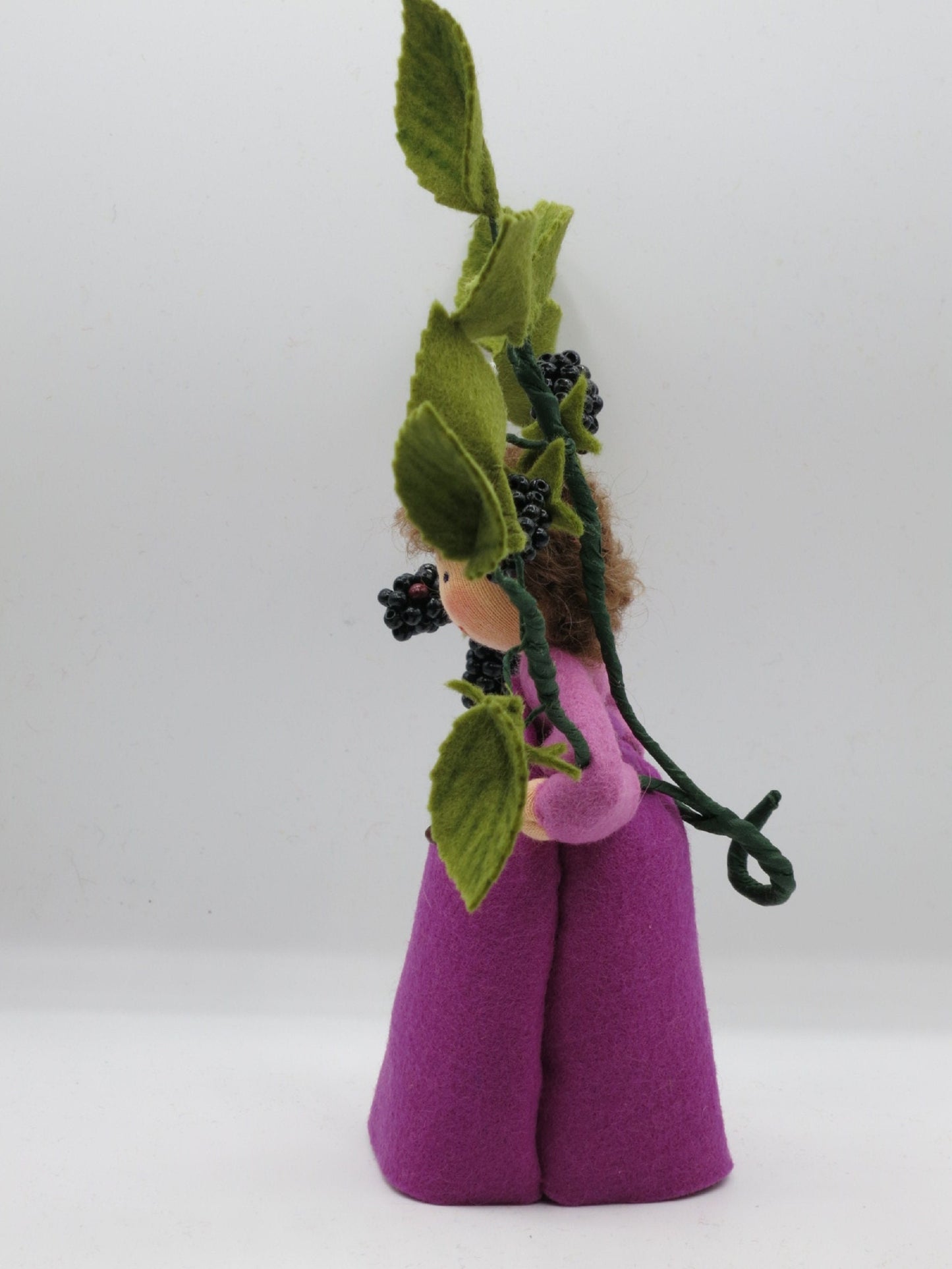 Profilansicht des Brombeer-Blumenkinds mit violettem Kleid und hoch aufragendem Zweig aus Filzblättern und Beeren.