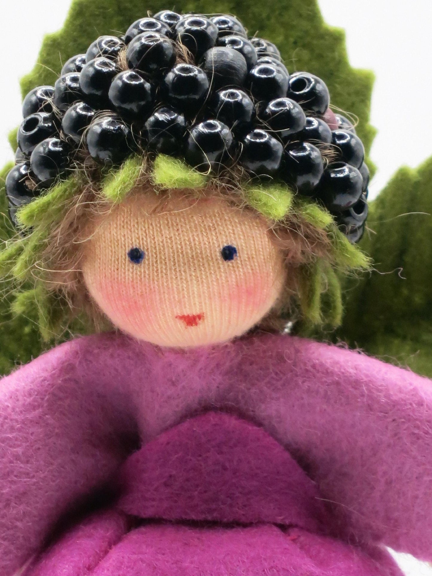 Porträt des Brombeer-Elfchens mit besticktem Gesicht, braunem Wollhaar und einem Kranz aus schwarzen Brombeeren.