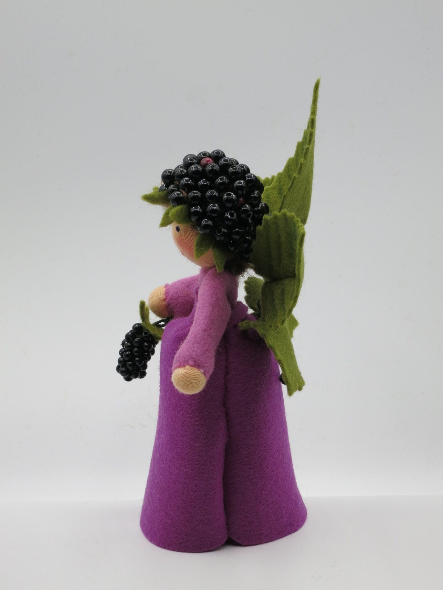 Profilansicht des handgefertigten Brombeer-Elfchens mit violettem Kleid, Brombeerzweig und großen grünen Filzblättern.