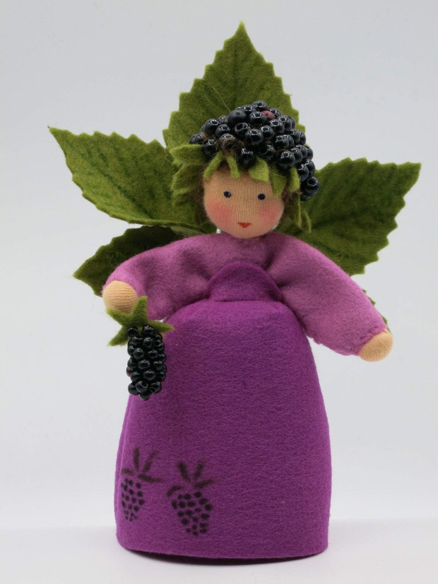 Gesamtansicht des Brombeer-Elfchens mit violettem Filzkleid, dunklen Beeren und fächerförmigen grünen Blättern.