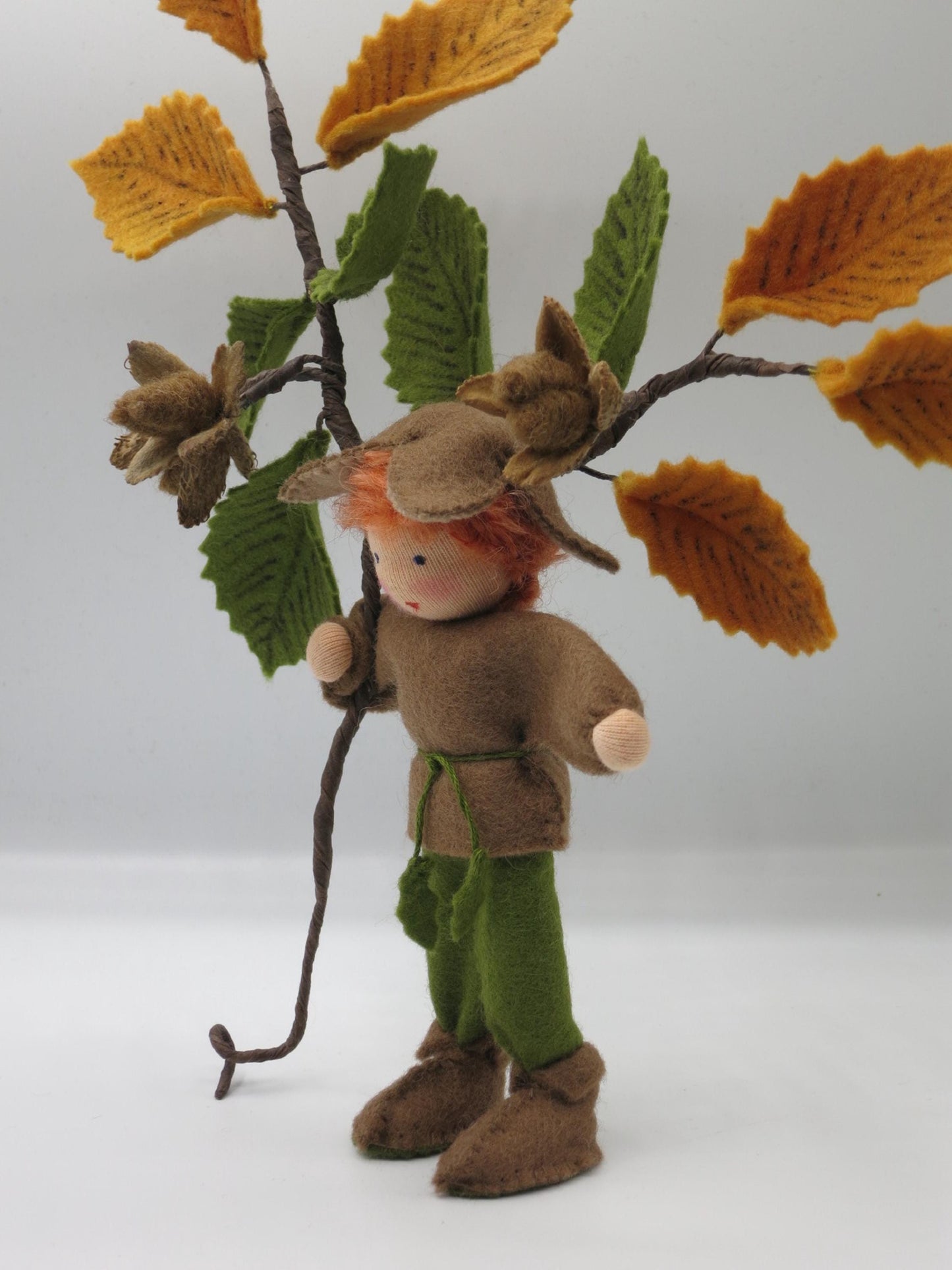 Dreiviertelansicht des Bucheckern-Jungen mit brauner Tunika, grüner Hose, Filzstiefeln und herbstlichem Buchenzweig.