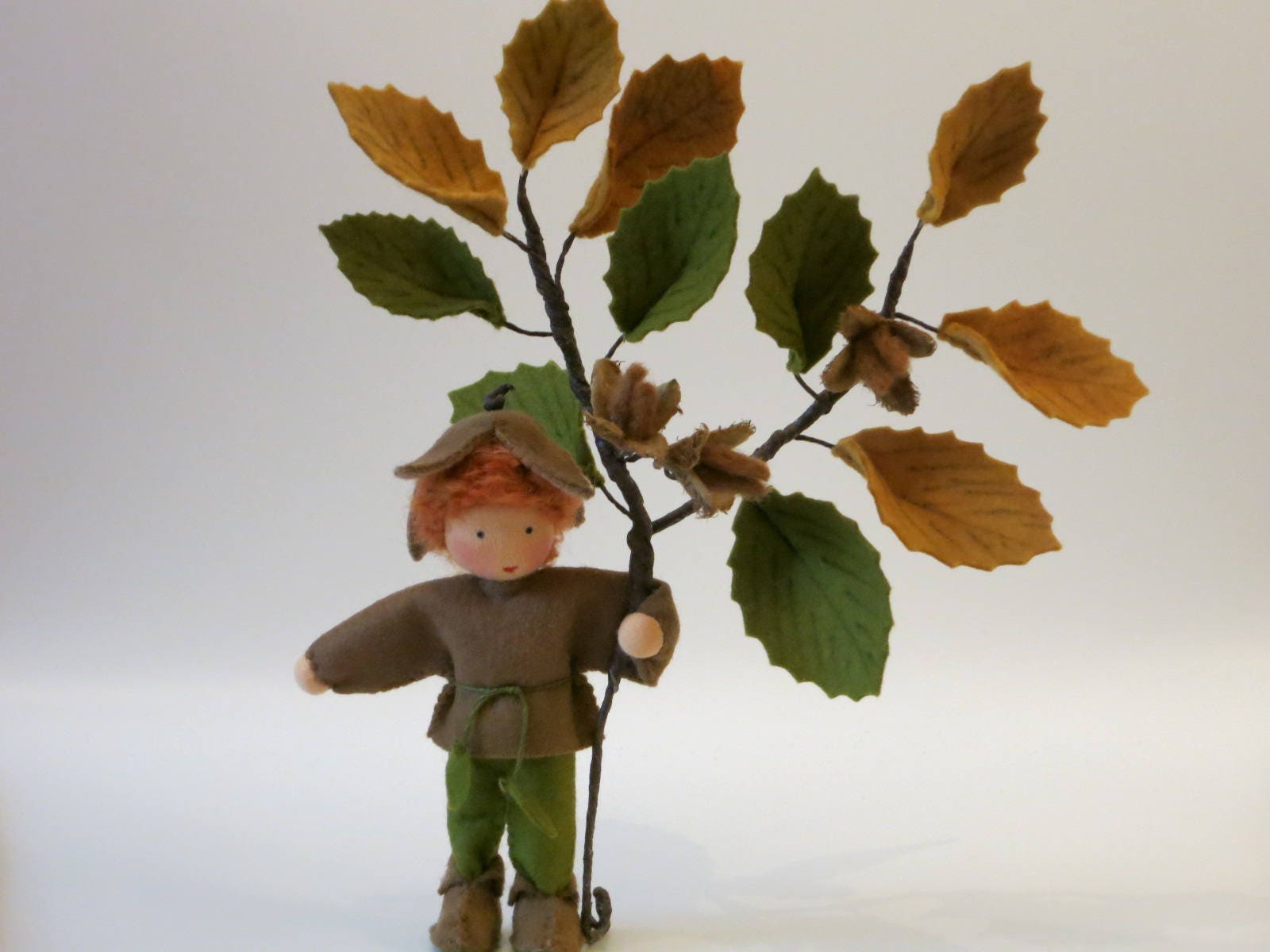 Handgefertigter Bucheckern-Junge mit braun-grüner Filzkleidung und großem Buchenzweig für den Herbst-Jahreszeitentisch.