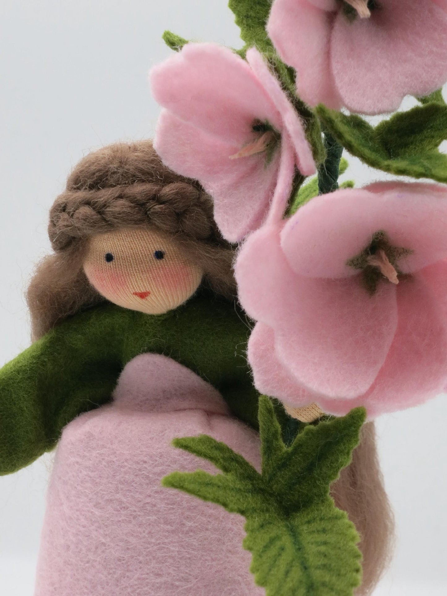 Detailaufnahme des Buschmalve-Blumenkinds mit Gesicht, braunem Flechthaar und handgearbeiteten rosa Filzblüten