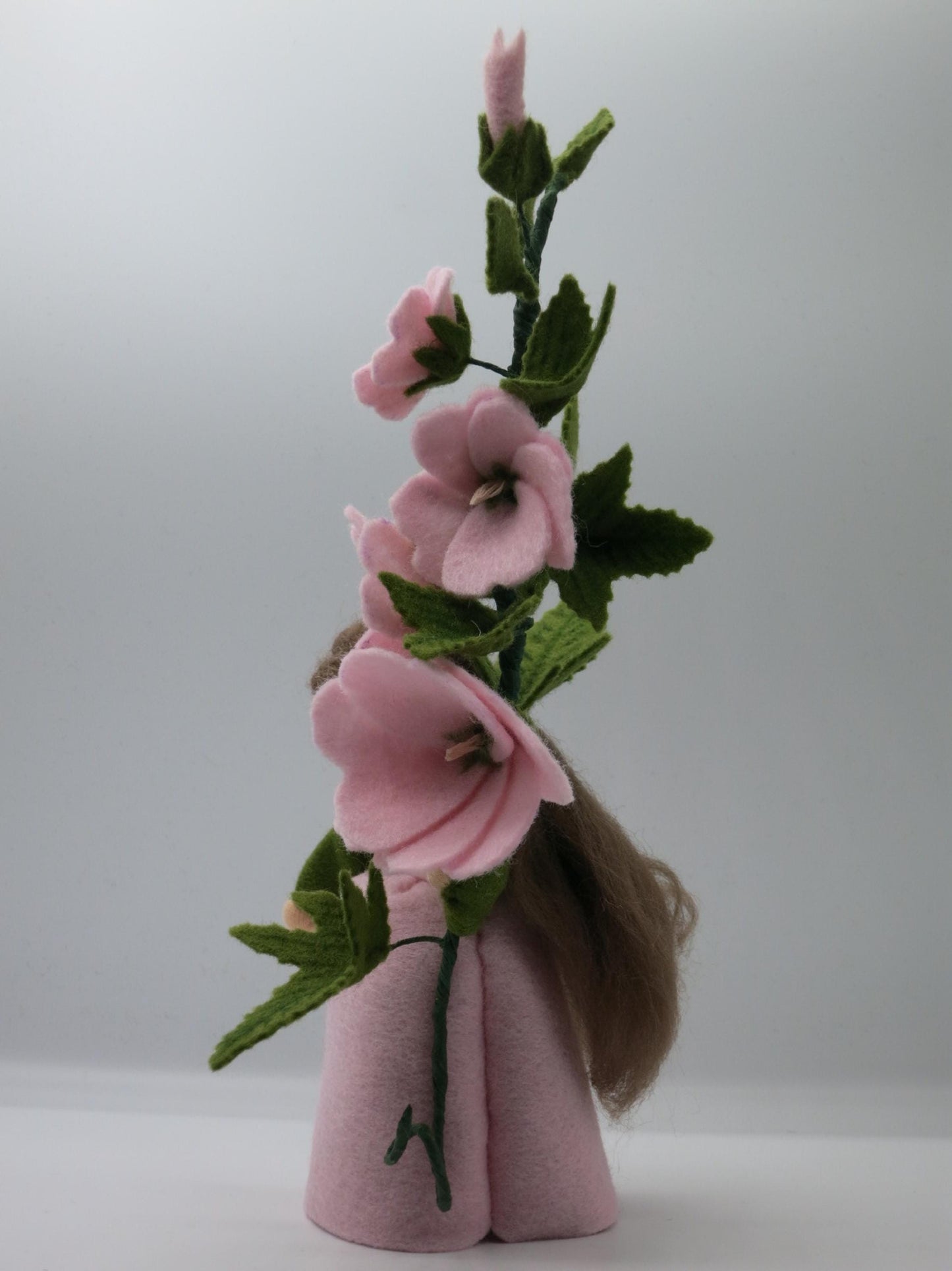 Rückansicht des Buschmalve-Blumenkinds mit langem braunem Wollhaar und rosa Blütenstiel aus Filz