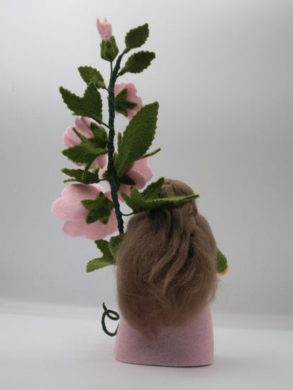 Buschmalve-Blumenkind von hinten mit langem braunem Wollhaar, rosa Filzkörper und blühendem Malvenzweig