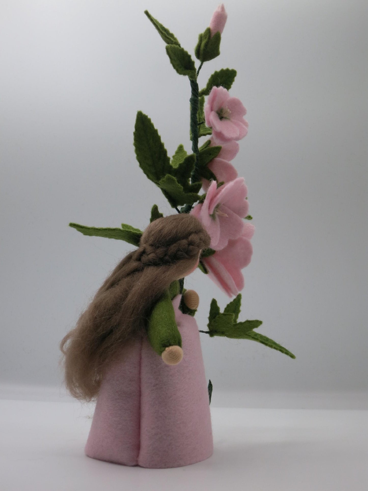 Seitliche Ansicht des handgefertigten Buschmalve-Blumenkinds mit rosa Filzblüten, grünen Blättern und Wollhaar