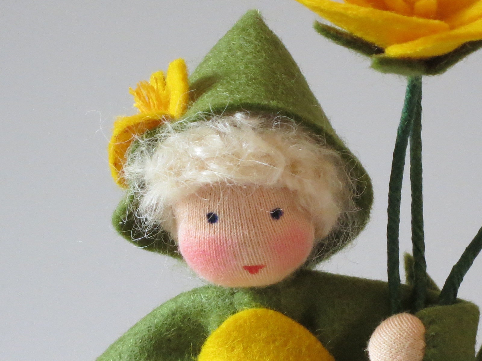 Porträt des Butterblumen-Blumenkinds mit blondem Wollhaar, grünem Filzhut und kleiner gelber Blüte